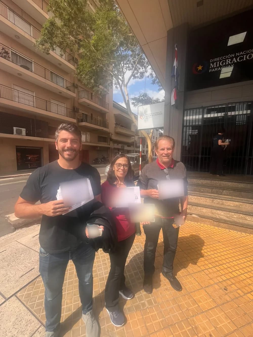 Gustavo, Rosa e Carlos Ribeiro com documentos da residência paraguaia em frente à Dirección Nacional de Migraciones, em Assunção; dados pessoais desfocados